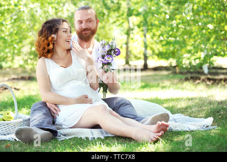 Schöner Mann gibt einen Blumenstrauß zu seinem schönen schwangere Frau im Park Stockfoto