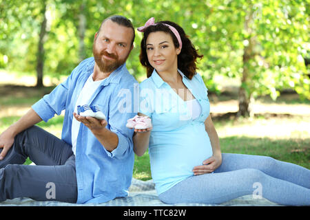 Schöne schwangere Frau mit ihren geliebten Mann mit Baby booties im Park Stockfoto