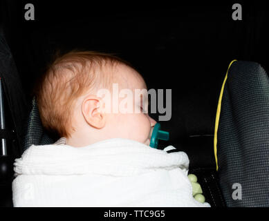 Rothaarige Baby schlafen in der Beförderung verpackt in einem bequemen Decke mit einem Schnuller Stockfoto
