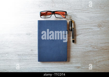 Arbeitsplatz - blau Notizbuch, Stift und Brillen auf grau Holz- Hintergrund Stockfoto