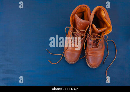 Alte Rot schmutzig hohe Schuhe auf blauem Hintergrund. Alte Schule vintage getragen Stiefel mit Lederbändern. Stockfoto