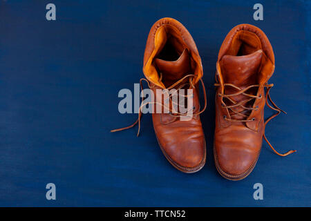 Alte Rot schmutzig hohe Schuhe auf blauem Hintergrund. Alte Schule vintage getragen Stiefel mit Lederbändern. Stockfoto