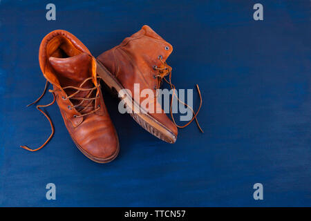 Alte Rot schmutzig hohe Schuhe auf blauem Hintergrund. Alte Schule vintage getragen Stiefel mit Lederbändern. Stockfoto
