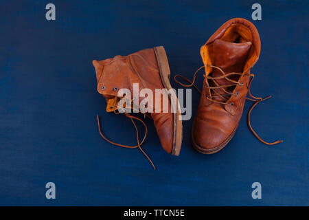 Alte Rot schmutzig hohe Schuhe auf blauem Hintergrund. Alte Schule vintage getragen Stiefel mit Lederbändern. Stockfoto