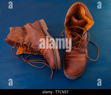 Alte Rot schmutzig hohe Schuhe auf blauem Hintergrund. Alte Schule vintage getragen Stiefel mit Lederbändern. Stockfoto