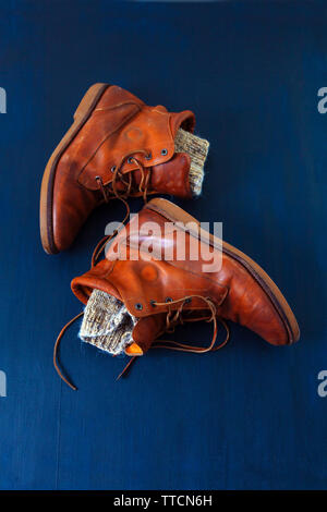 Alte Rot schmutzig hohe Schuhe auf blauem Hintergrund. Alte Schule vintage getragen Stiefel mit Lederbändern und Wolle gestrickt warm grey Socken. Stockfoto