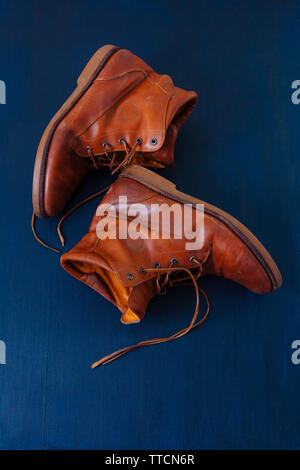 Alte Rot schmutzig hohe Schuhe auf blauem Hintergrund. Alte Schule vintage getragen Stiefel mit Lederbändern. Stockfoto