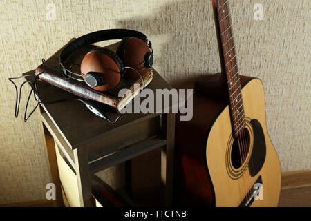 Akustik Gitarre stützte sich an der Wand mit Hocker und Kopfhörer im Zimmer, in der Nähe Stockfoto