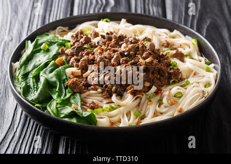 Würzige Dan Dan Nudeln mit Hackfleisch und Kräutern mit heißer Soße in einem Teller auf dem Tisch. Horizontale Stockfoto