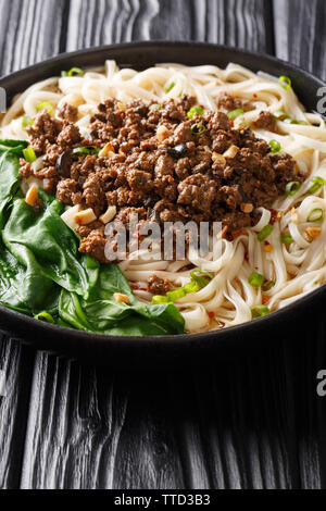 Dan Dan Nudeln - herzhaft und würzig Sichuan Nudeln serviert mit Hackfleisch Nahaufnahme auf dem Teller auf dem Tisch. Vertikale Stockfoto