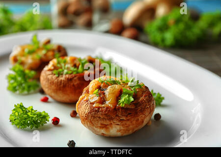 Gefüllte Champignons auf Platte, am Tisch Hintergrund Stockfoto