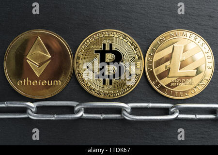 Physische Bitcoin, Litecoin und des Astraleums Gold Münzen auf einen schwarzen Stein Schiefer Platte mit Kette. Cryptocurrency blockchain abstraktes Konzept. Stockfoto