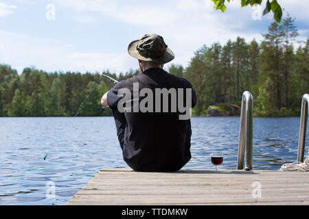 Reifer Mann angeln vom hölzernen Pier in der Nähe von Ferienhaus am See in Finnland im Sommer Stockfoto