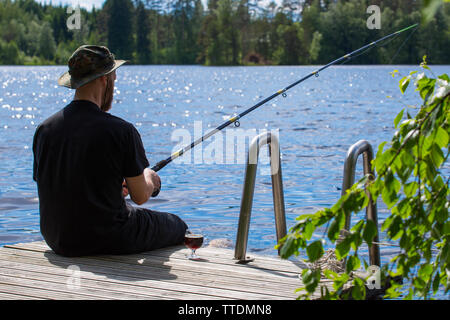 Reifer Mann angeln vom hölzernen Pier in der Nähe von Ferienhaus am See in Finnland im Sommer Stockfoto