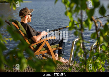 Reifer Mann angeln vom hölzernen Pier in der Nähe von Ferienhaus am See in Finnland im Sommer Stockfoto