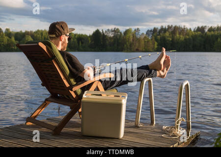 Reifer Mann angeln vom hölzernen Pier in der Nähe von Ferienhaus am See in Finnland im Sommer Stockfoto