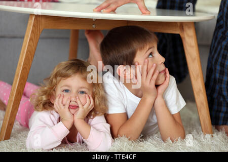 Süße kleine Kinder spielen unter dem Tisch Stockfoto