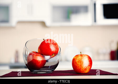 Äpfel in eine Glasschüssel auf Holztisch, aus der Nähe. Stilvolle Küche Interieur. Stockfoto
