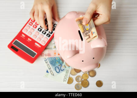 Die Frau Hände die Euro-Banknoten in einem Sparschwein und zählen mit Rechner auf dem Tisch. Finanzielle Einsparungen Konzept Stockfoto