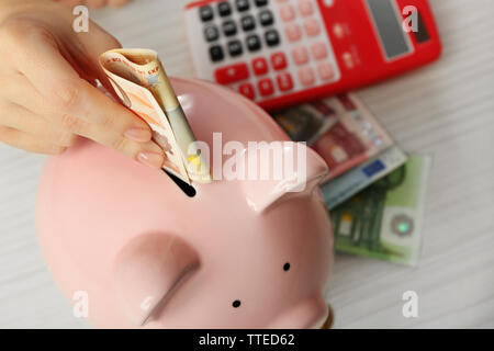 Die Frau Hände, Banknote in ein Sparschwein auf den Tisch. Finanzielle Einsparungen Konzept Stockfoto