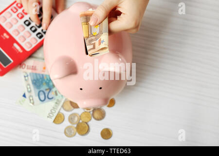 Die Frau Hände die Euro-Banknoten in einem Sparschwein und zählen mit Rechner auf dem Tisch. Finanzielle Einsparungen Konzept Stockfoto