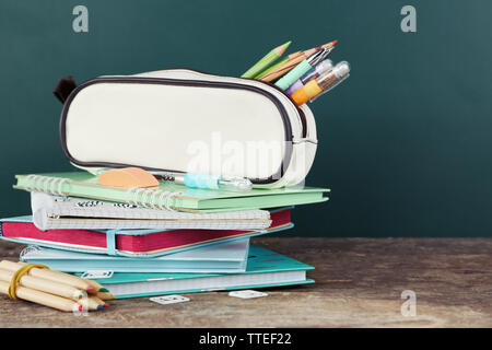Federmäppchen mit verschiedenen Schreibwaren auf alten Holztisch, auf blackboard Hintergrund Stockfoto