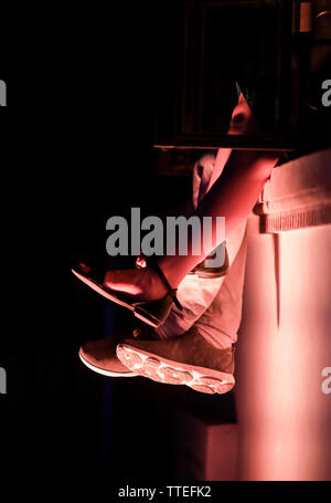 Details mit den Füßen auf ein junges Paar (sie Sandalen und seine Turnschuhe), sitzt auf einem Stein Leiste, in der Nacht und mit einem starken Kontrast. Stockfoto