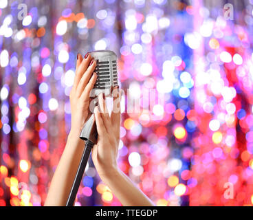 Weibliche Hände halten Mikrofon gegen helles glitzern Hintergrund Stockfoto