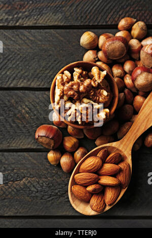 Ein Löffel aus Holz, eine Schale, Haselnüsse, Walnüsse, Mandeln und Eicheln auf dem hölzernen Tisch Stockfoto