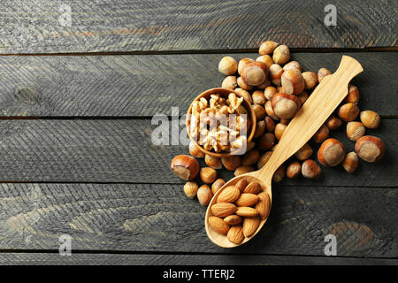 Ein Löffel aus Holz, eine Schale, Haselnüsse, Walnüsse, Mandeln und Eicheln auf dem hölzernen Tisch Stockfoto