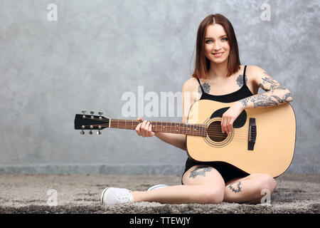 Attraktive Frau mit tattoo Gitarre spielen auf grauem Hintergrund Stockfoto