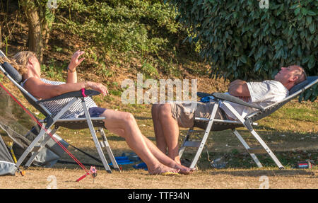 Ein Paar mittleren Alters, die außerhalb in der heißen Sonne auf den Liegestühlen, neben ihr Zelt auf einem Campingplatz in England, Großbritannien. Stockfoto