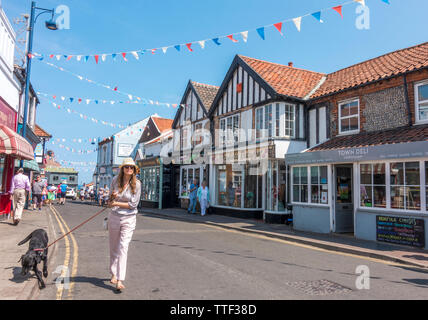 Frau Gehen ein Hund, und Bunting kreuz und quer über eine Hauptstraße in Sheringham Town Center an einem heißen Sommertag mit blauem Himmel. North Norfolk, England, UK. Stockfoto