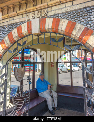 Alter Mann in Sheringham Town Center vermeiden die Hitze an einem heißen Sommer Tag, innerhalb der historischen Uhr Gebäude von 1862. North Norfolk, England, UK. Stockfoto