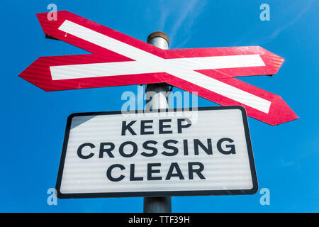 Ein bahnübergang (wo eine Straße überquert eine Eisenbahnlinie) Wegweiser, mit dem Hinweis - Halten Kreuzung klar, gegen einen blauen Himmel. Norfolk, England, UK. Stockfoto