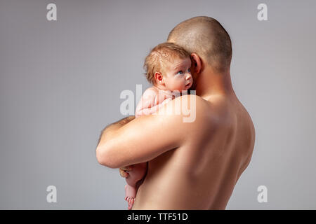 Porträt eines neugeborenen Jungen, Alter 1 Monat, rote Haare, blaue Augen, der Vati, der in seinen Armen hält, fest Knuddel und lächelt. Das Konzept der Familie, Liebe Stockfoto