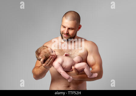 Porträt eines neugeborenen Jungen, Alter 1 Monat, rote Haare, blaue Augen, der Vati, der in seinen Armen hält, fest Knuddel und lächelt. Das Konzept der Familie, Liebe Stockfoto
