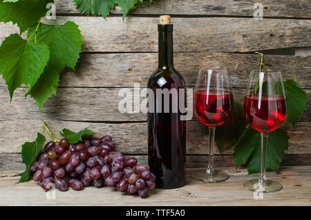 Der Weinstock eine Flasche Wein und zwei Gläser mit Rotwein auf Holz- Hintergrund mit Lichtstrahlen Stockfoto