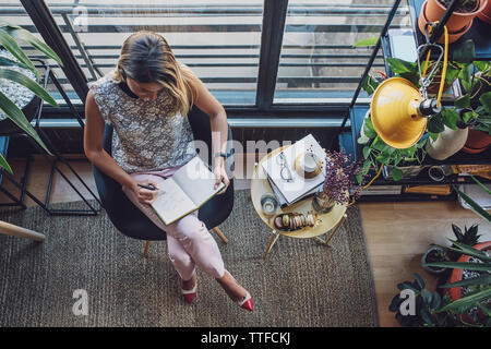 Draufsicht der Geschäftsfrau in Tagebuch zu schreiben, während Sie sitzen auf Stuhl zu Hause Büro Stockfoto