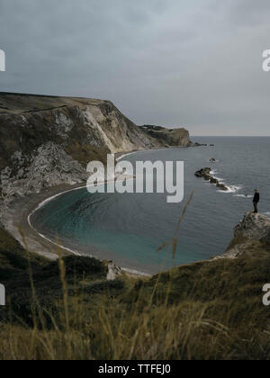 Ein Mann steht auf einem Felsen auf dem Hintergrund der Bucht Durdle Door Stockfoto