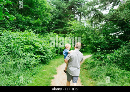 Ansicht der Rückseite ein Vater seinen Sohn auf einen Weg in einer Stadt park Stockfoto