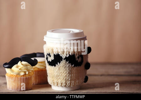 Becher mit Deckel und leckere Cupcakes mit Schnurrbart auf unscharfen Hintergrund Stockfoto