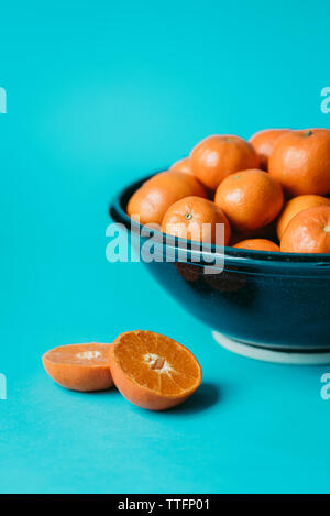 Mandarin Orange in der Hälfte durch eine Schale von Orangen auf blauem Hintergrund. Stockfoto