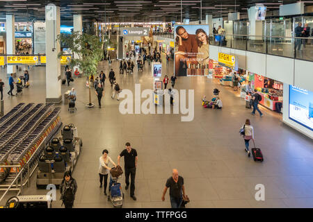 Ansicht der Bahnhofshalle o fDeparture Lounge 2 am Flughafen Schiphol, Amsterdam, mit Reisenden, Shops, Werbung, Trolleys, Hilfe Buggys. Stockfoto