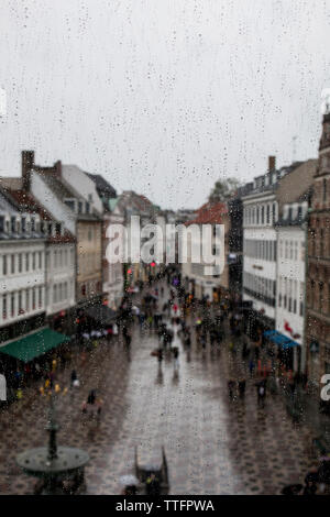 Menschen auf Wanderweg inmitten von Gebäuden durch nasse Fenster während der regnerischen Jahreszeit gesehen Stockfoto