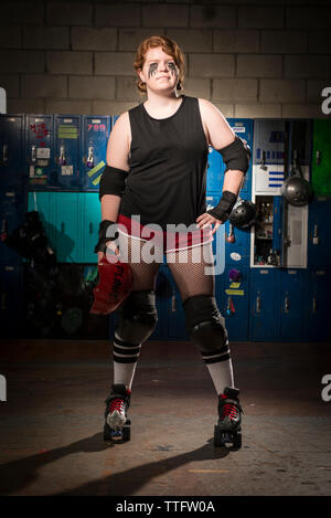 Portrait von zuversichtlich Sportlerin mit der Hand auf der Hüfte tragen Rollschuhe im Stehen gegen Schließfächer Stockfoto