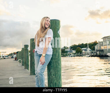 Glückliche Frau schreien beim Stehen auf Pier über Fluss gegen Himmel bei Sonnenuntergang Stockfoto