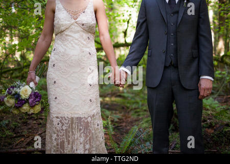 Mittelteil des Brautpaar Händchen beim stehen auf Feld im park Stockfoto