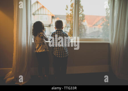 Ansicht der Rückseite des Geschwister durch Fenster zu Hause stehend Stockfoto