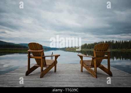 Stühle aus Holz auf Pier über den See gegen bewölkter Himmel Stockfoto
